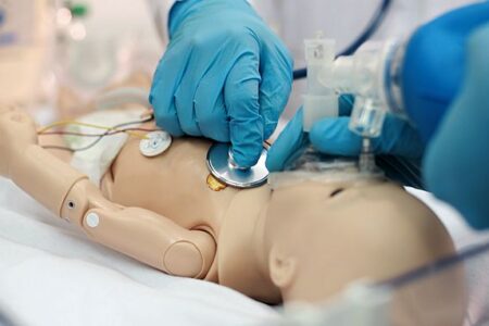 Image of gloved physician hands performing exam on pediatric manakin.