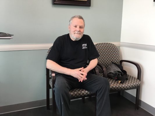 Alan Cirlin sitting in a chair and smiling with his hands interlaced.