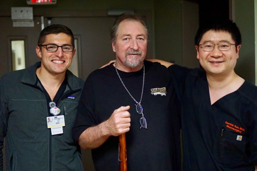 Rocky Buchanan standing with Dr. Sun and a neurosurgery resident, smiling during a clinic visit.