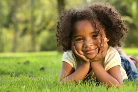 A happy-looking child sitting in the grass.