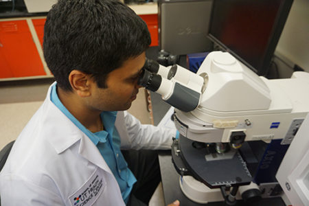 Someone looking at a microscope inside a lab setting.