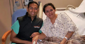 Dr. Ramesh Grandhi sitting with a patient in a hospital bed and smiling.