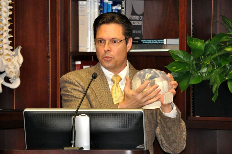 A presenter for the 2012 Craniosynostosis Workshop standing at a podium holding a cranial molding helmet.