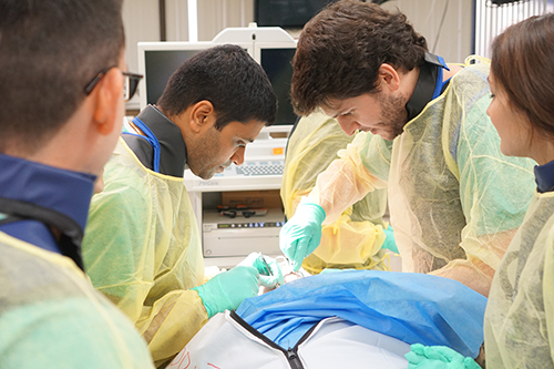 People standing around a cadaver with medical instruments.