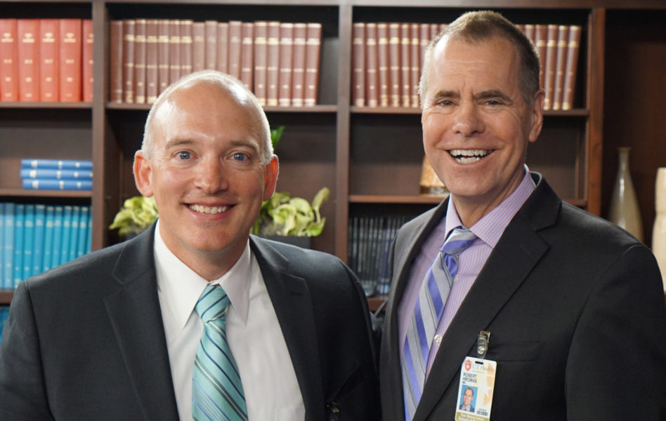 Dean Robert Hromas, M.D., FACP, smiling and standing next to Dr. John Floyd in the Department of Neurosurgery conference room.