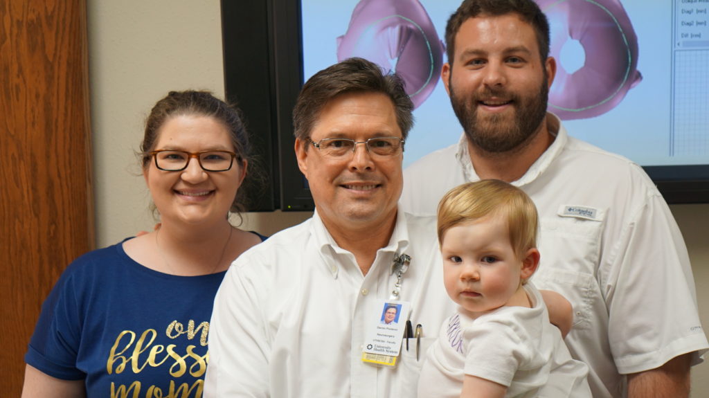 Cranial Remolding Clinical Director Darren Poidevin smiles while holding patient Adley Stubbs. Darren is flanked by Adeley's smiling parents.