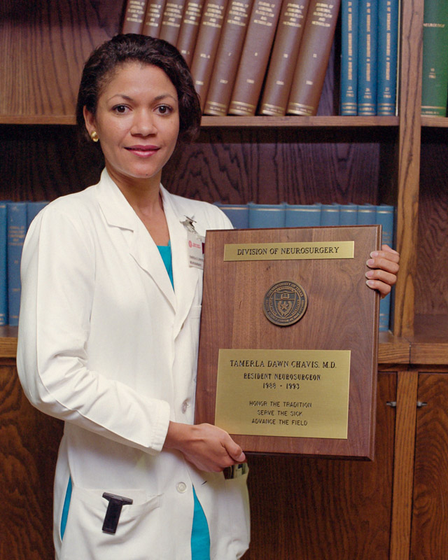 Dr. Tamerla Chavis standing in a white coat holding her graduation plaque.