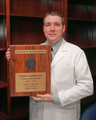 Dr. Glenn Harper standing in a white coat holding his graduation plaque.