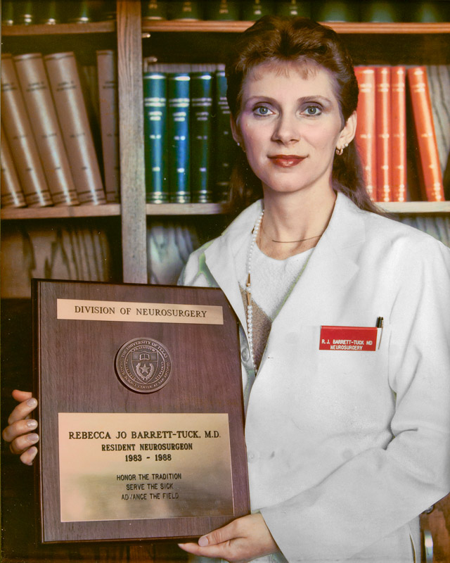 Dr. Rebecca Barrett-Tuck standing in a white coat with her graduation plaque.