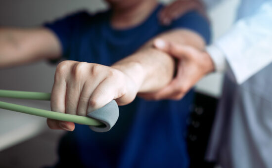 Asian male physical therapist descent working with patient doing stretching exercise with a flexible exercise band in clinic room.