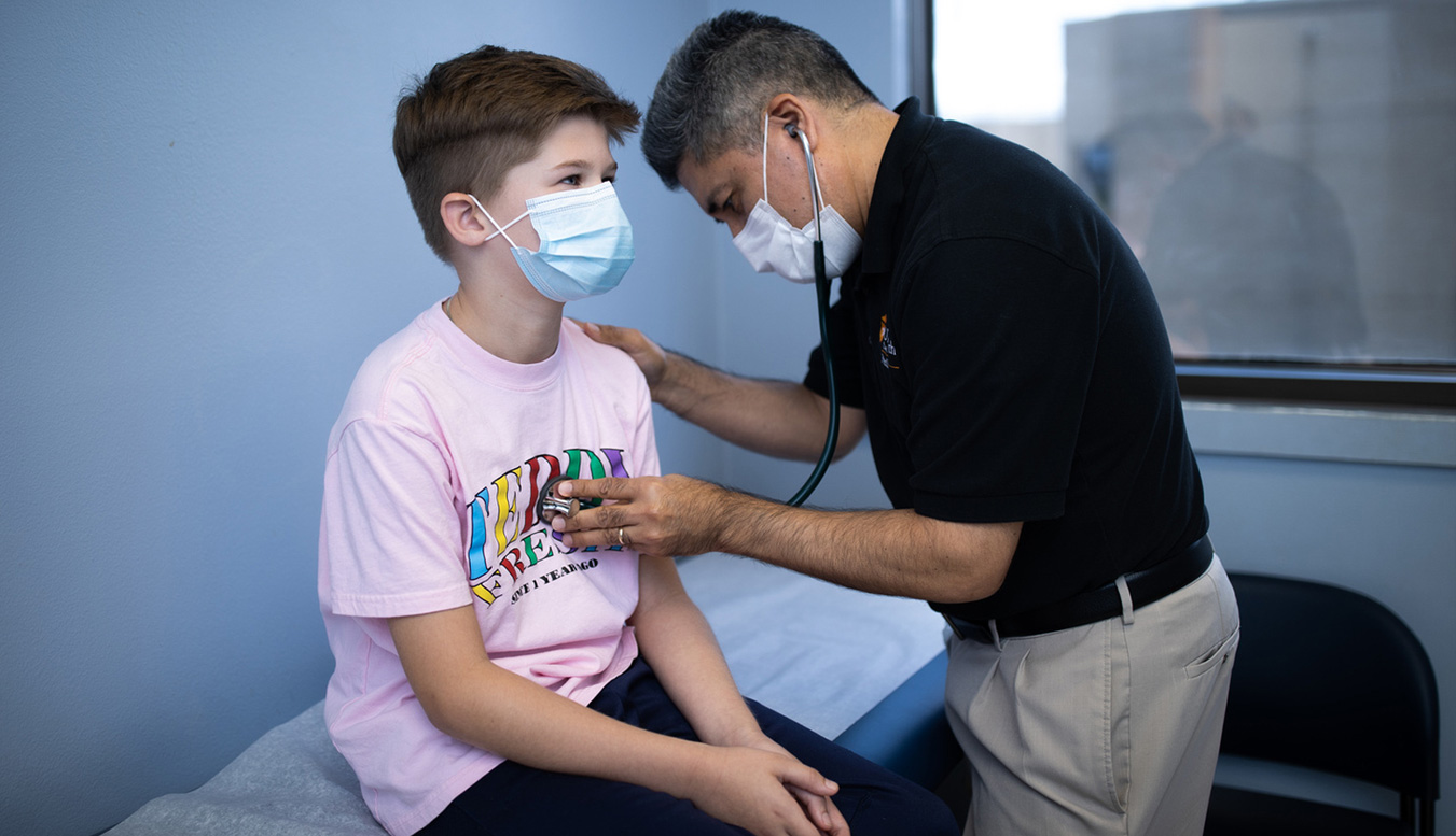 Young male patient and doctor examining him with a stethoscope while both wear germ free masks